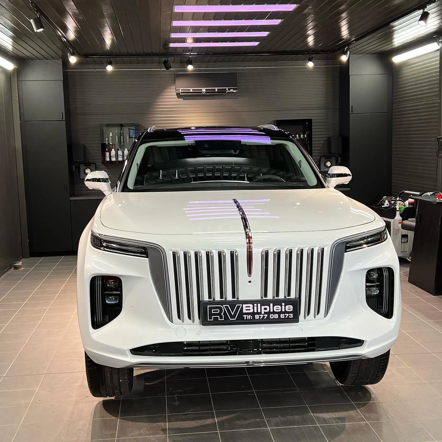 Hvit Hongqi E-HS9 i studioet til RV Bilpleie, med RV Bilpleie-skilt foran